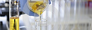 Hand in rubber glove pours yellow liquid into flask in chemical laboratory closeup