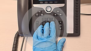 Hand in rubber glove pushes buttons on a modern phone in the office