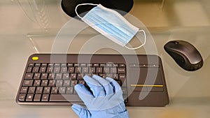 A hand in rubber glove on wireless keyboard on glass office desk