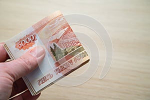 Hand with Russian rubles on a blurred wooden background, five thousand rubles banknotes rolled up in hand. A large bundle of money