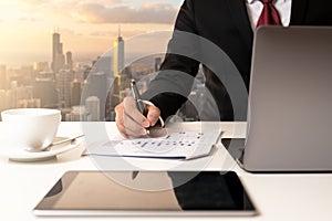 Hand`s businessman holding pen and analysis data chart on document paper and looking computer at modern office city of chicago.