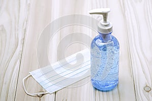 Hand sanitizer bottle or alcohol gel and surgical face mask on wooden table with cpoy spcae