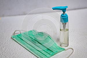 Hand sanitizer bottle and surgical mask on white surface in vertical design. General personal protective equipment for use in