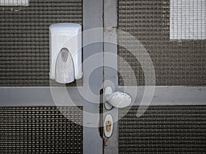 Hand sanitizer dispenser mounted on the wall of entrance door with a lock and knob, in public place, a residential building