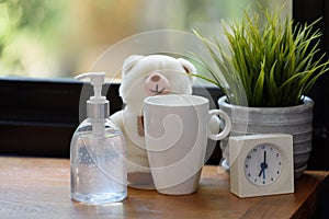 Hand sanitizer,white cup,teddy bear and alarm clock on wood table with green nature background while Covid-19  home quarantine photo