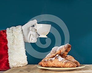 Hand of Santa Claus with a cup of coffee on a turquoise background. Delicious winter breakfast