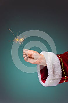 Hand of Santa Claus holding a sparklers on blue background