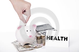 Hand saving money in piggy bank for message health.