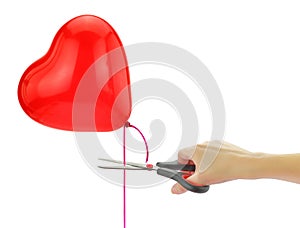 Hand with a scissor cutting a red heart shape balloon ribbon isolated on white Î’reaking up, separation concept