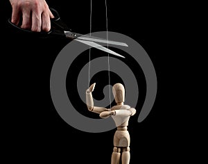 Hand with scissors cutting strings holding puppet. Independence, liberation from slavery, control, abuse cessation