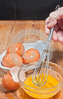 Hand scrambling egg in glass bowel with whisk, egg shells