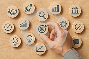 Hand selecting target icon among multiple round wooden business icons, symbolizing strategy, decision making, focus and photo