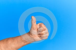 Hand of senior hispanic man over blue isolated background doing successful approval gesture with thumbs up, validation and