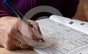 Hand of senior person doing crosswords puzzle`s in a notebook. Leisure and free time