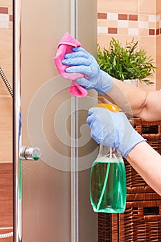 Hand of senior woman cleaning glass shower using microfiber cloth and detergent, household duties concept
