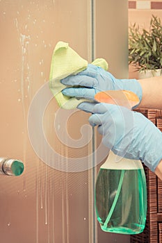 Hand of senior woman cleaning shower using green microfiber cloth and detergent, household duties concept