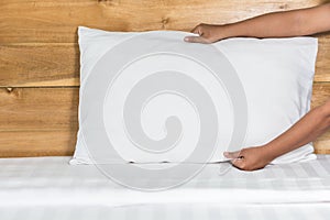 Hand set up white pillow on bed sheet in hotel room