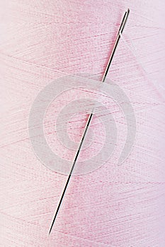 Hand sewing needle in pink thread spool