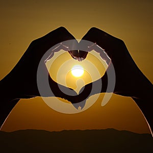 Hand shaped heart against sunset