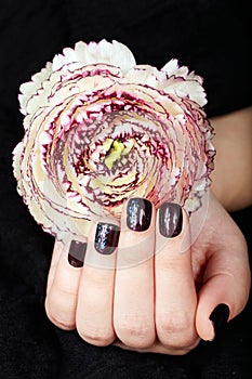 Hand with short manicured nails colored with dark purple nail polish and flower