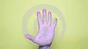 Hand showing palm or high five gesture isolated on yellow background