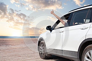 Hand showing thumb up out window car on blue sky, white clouds, sun and sea background