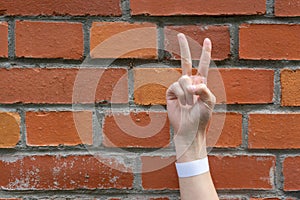 Hand shows with fingers the sign Victoria on a brick wall background. A sign of fortitude, victory and confrontation