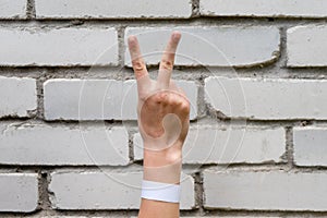 Hand shows with fingers the sign Victoria on a brick wall background. A sign of fortitude, victory and confrontation