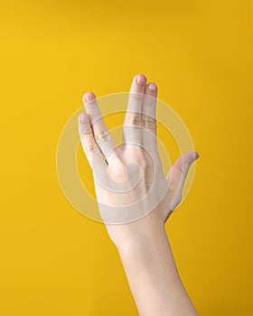 Hand shows Vulcan salute on yellow background. Hand gesture that means Live long and prosper