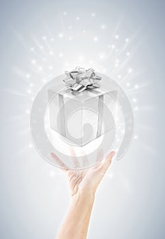 Hand with silver gift box and magic twinkles
