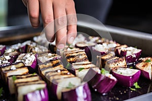 hand skewering grilled eggplant cubes for kabobs