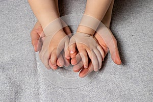 Baby little hands in gentle mother`s parental hands on a gray light background.