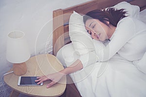 Hand of sleepy woman waking up with alarm clock on mobile phone.