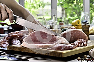 Hand slicing fresh raw pork meat on a cutting board in the kitchen
