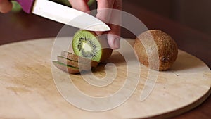 Hand slicing a kiwi with a knife on wooden board.