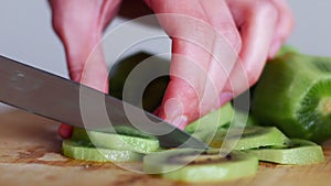 Hand slicing a kiwi with a knife on wooden board, close up, 4k