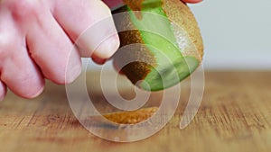Hand slicing a kiwi with a knife on wooden board, close up, 4k