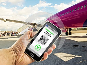 Hand with a smartphone with the digital green pass of the european union and the QR code near plane boarding