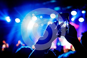 Hand with a smartphone records live music festival and taking photo of concert stage.