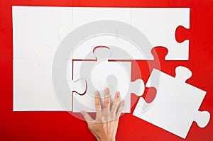 Hand solving a puzzle piece on red background