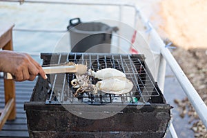 Hand of someone are gril fresh squid on hot stove with ice tong