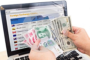 Hand sorting USD and Yuan in front of currency exchange chart on