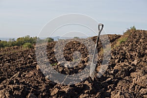 a hand spade stands in a freshly plowed field