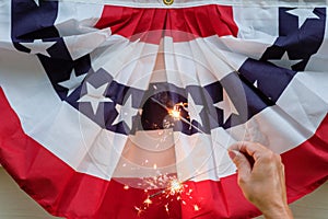 Hand with sparklers in front of a red white and blue bunting flag