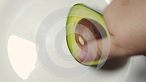 Hand spining avocado on the white plate. Slow motion