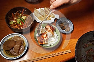 Hand with a spoon puts a piece of salmon fillet into a bowl of rice at a Japanese diner with many bowls