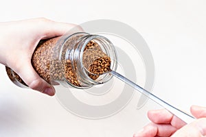 Hand spooning up instant coffee from glass jar