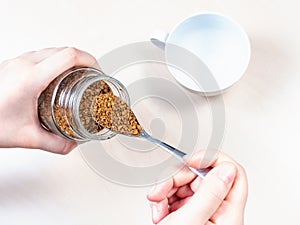 Hand spooning up instant coffee from jar over cup