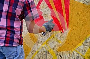 A hand with a spray can that draws a new graffiti on the wall