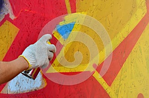 A hand with a spray can that draws a new graffiti on the wall